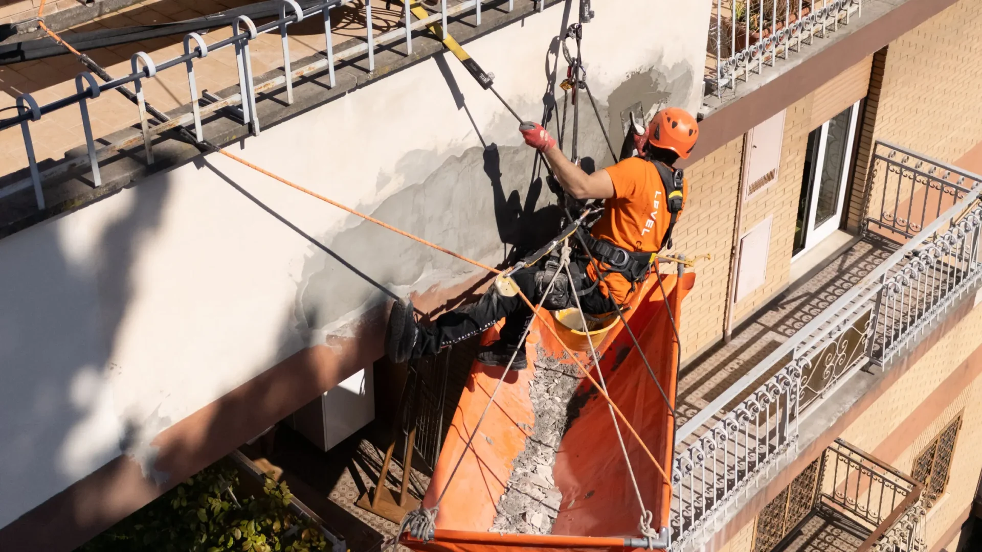 Técnico de Level On reparando el revestimiento exterior de un edificio residencial mediante acceso por cuerda.