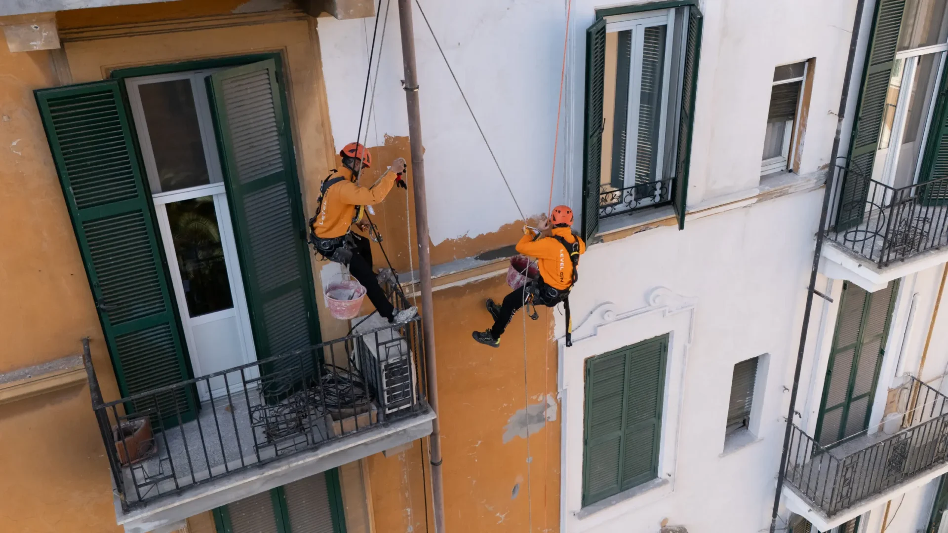 Dos técnicos de Level On realizan trabajos de reparación y pintura en la fachada de un edificio residencial mediante acceso por cuerda.